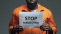 Stop persecution phrase on cardboard in hands of Afro-American prisoner, assault