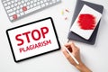 Stop plagiarism concept. Office desk table with keyboard, paper notebooks, tablet. Message STOP PLAGIARISM on tablet screen