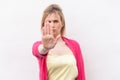 Stop. Portrait of serious blond young woman in yellow shirt and red blouse standing, showing stop gesture with hand. focus on hand