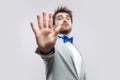 Stop. Portrait of serious handsome bearded man in casual grey suit, blue bow tie standing with rejecting stop hand and try to