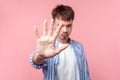 Stop! Portrait of young serious brown-haired man with small beard and mustache gesturing stop. isolated on pink background