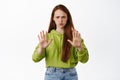 Stop right there. Angry and serious redhead woman stretch hand to block, refuse action, prohibit and reject person