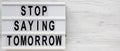 `Stop saying tomorrow` words on a modern board on a white wooden surface, top view. Overhead, from above, flat lay. Copy space