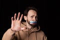 Close-up portrait of young emotive man with three colors duct tape over his mouth isolated on dark background Royalty Free Stock Photo