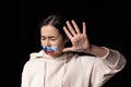 Half-legth portrait of young emotional upset girl with three colors duct tape over her mouth isolated on dark background Royalty Free Stock Photo