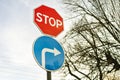 Stop sign and road sign turn to the right against a blue sky and a tree Royalty Free Stock Photo