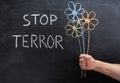 STOP TERROR on a chalkboard, three flowers drawn in chalk in a man`s hand