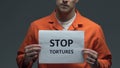 Stop tortures phrase on cardboard in hands of Caucasian prisoner, protest