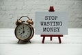 Stop Wasting Money text and alarm clock on white brick wall and wooden background Royalty Free Stock Photo