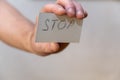 Stop. A word written in jagged letters. A man`s hand holds a white paper rectangle with text against a gray background