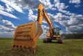 A stopped yellow excavator in a field and a beautiful sky