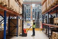 Storehouse employee in uniform working on forklift in modern automatic warehouse. Boxes are on the shelves of the warehouse.