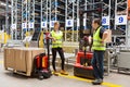 Storehouse employees in uniform standing near pallet truck and forklift in modern automatic warehouse.Boxes are on the shelves of Royalty Free Stock Photo