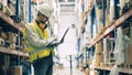 Storeman in uniform typing on laptop among warehouse shelves