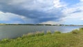 A storm cloud hangs over the lake and it is raining. The water ripples in the wind. In summer, meadow flowers bloom on the grassy Royalty Free Stock Photo