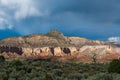 Storm clouds and faint rainbows over a desert mountain peak with colorful cliffs highlighted by the light of sunset Royalty Free Stock Photo