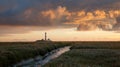 Storm clouds at sunset over the lighthouse of Westerhever. In the foreground a small channel leads into the picture Royalty Free Stock Photo