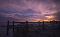 Storm damaged dock at the beach with pink and orange sunset clouds