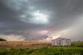 Storm and wall cloud with lightning bolt behind an old farm building.