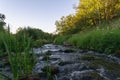 stormy brook with rapids, flowing among meadows and forests. evening sunset in summer. Royalty Free Stock Photo