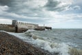 A stormy day at the beach with a wooden structure extending into the rough sea, with the waves crashing on the pebbled beach Royalty Free Stock Photo