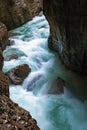Stormy mountain stream with clear blue water flows down a rocky gorge in Partnachklamm in Germany. Sunlight penetrates Royalty Free Stock Photo
