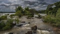 A stormy river flows along a rocky bed. Water foams around boulders.