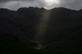 Stormy skies and a bright sun trace light over The Langdale Pikes in the English Lake District