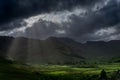 Stormy skies and a bright sun trace light over The Langdale Pikes in the English Lake District