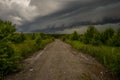 Stormy sky, low thunderclouds hanging over the dirt road leading into the forest Royalty Free Stock Photo