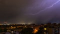 Stormy sky raining with a huge lightning bolt drawing a diagonal in the sky on the outskirts of a city over buildings