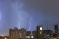 Stormy sky with several huge lightning bolts striking the ground on the outskirts of a city over buildings