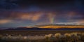 Stormy Sunset with rain and rainbow in the desert with light on mountain range. Royalty Free Stock Photo