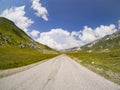 Straight asphalt road surrounded by mountains with clouds in the background