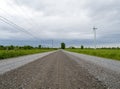 Straight gravel road landscape with a wind turbine and power lines Royalty Free Stock Photo