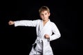 Straight karate arm hit. Kid in brand new kimono looking on the camera on black background