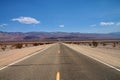 Straight road through a flat desert landscape, with hills and a blue sky Royalty Free Stock Photo