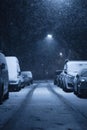 Straight road between parked cars at a snowing night