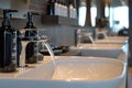 A straight row of sinks with soap dispensers attached to them in a well-lit room, A close-up of a hair washing station with modern