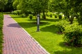 Straight stone tile pavement in a park landscaped with green grass and bushes.