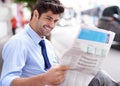 Straight to the business section. A handsome young businessman reading a newspaper while sitting on a bench in the city.