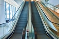 Straight on view of ascending escalators beside illuminated staircase in generic business setting
