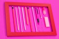 Straightly arranged group of pink color writing equipment lying in red photo frame on pink surface isolated