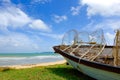 Stranded fisherman boat on green grass toward seaview at sunny day and cloudy blue sky