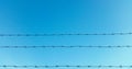 Strands of barbed wire with blue sky and clouds in the background Royalty Free Stock Photo