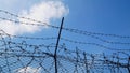 Strands of barbed wire with spikes above metal fence with blue sky with clouds. conceptual image