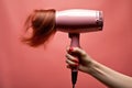 Strands of hair flow from the grip of a woman's hand holding a blow dryer, capturing the essence of untamed locks Royalty Free Stock Photo