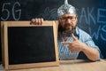 A strange bearded conspiracy theorist in a protective aluminum foil hat and glasses sits at a table and points his