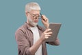 Strange content. Surprised albino man in glasses looking in digital tablet and reading news on turquoise background