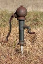 Strange and unusually shaped vintage retro partially rusted wrought iron dark green hand water pump mounted on water pipe Royalty Free Stock Photo